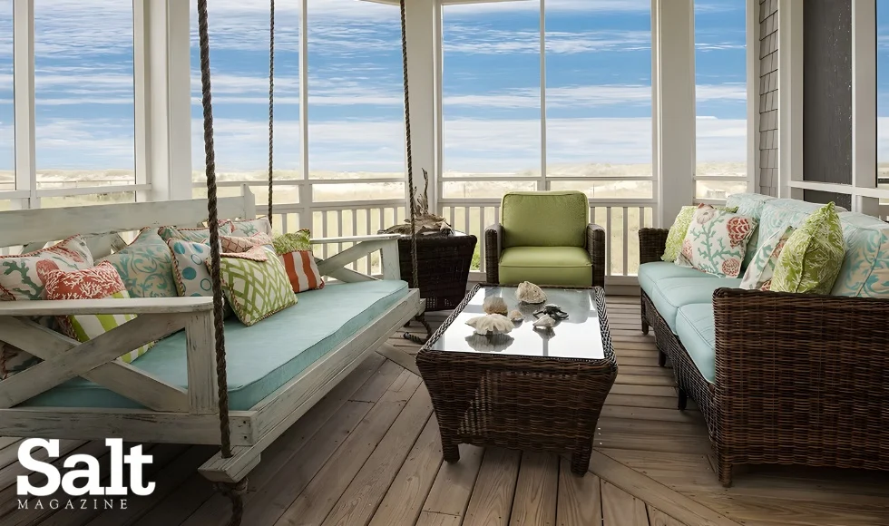Coastal porch with rattan furniture, colorful cushions, and ocean view, showcasing Interior Design Wilmington, NC. Glass-top table with shells.